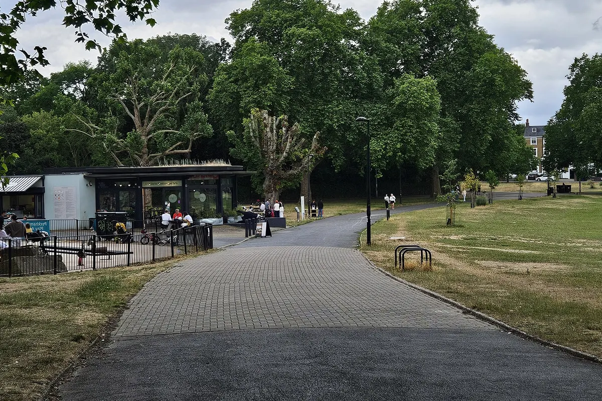 A path and lawns with a park cafe among trees in Peckham Rye Park